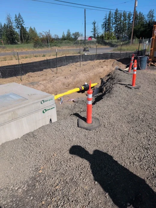 Construction site excavation with exposed utility pipe and traffic delineators showing open trench safety hazards