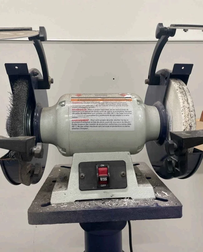 Bench grinder workstation with missing wheel guards and worn abrasive wheels showing OSHA safety violations
